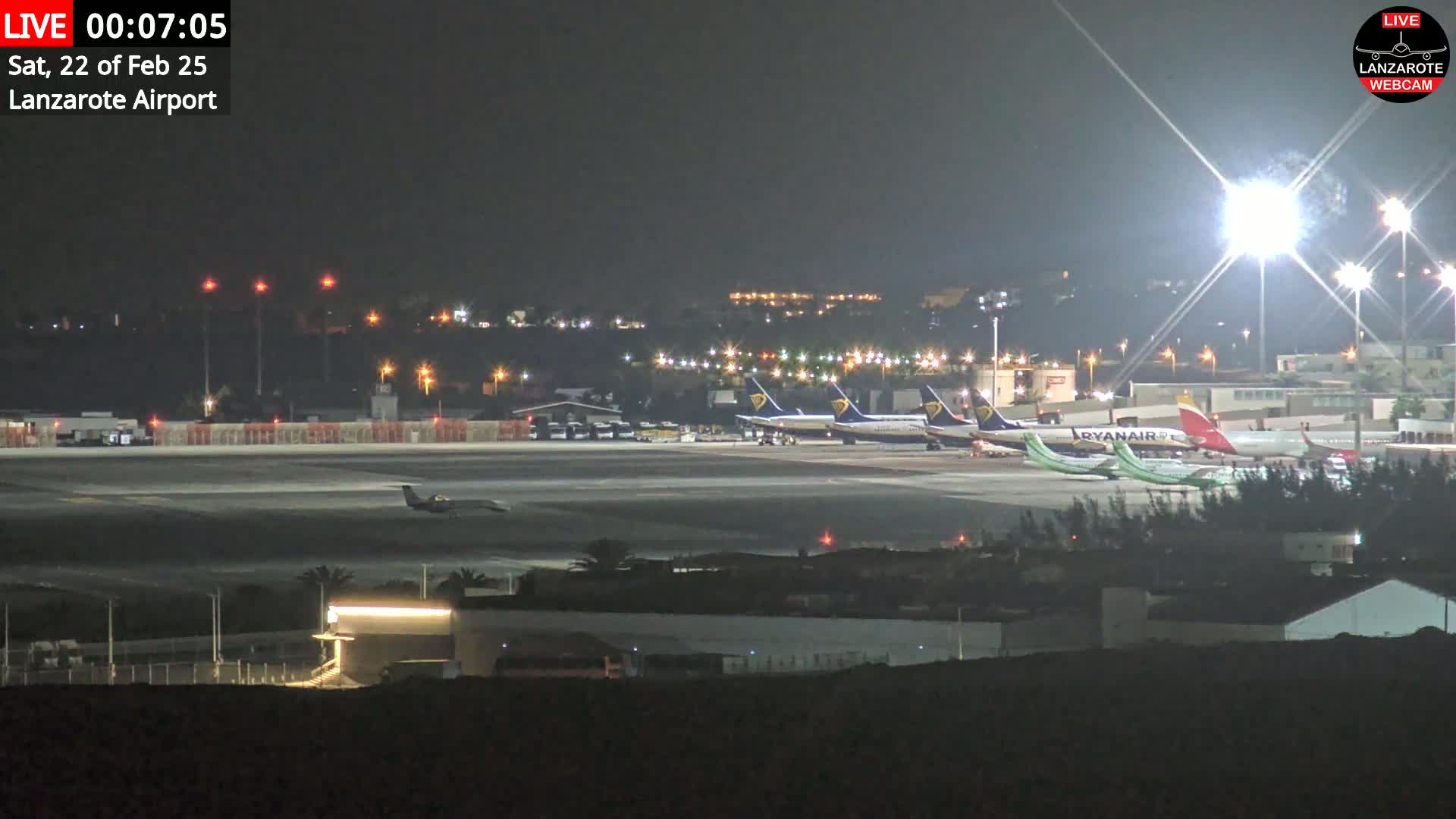 Several airplanes are parked on a brightly lit tarmac at night.