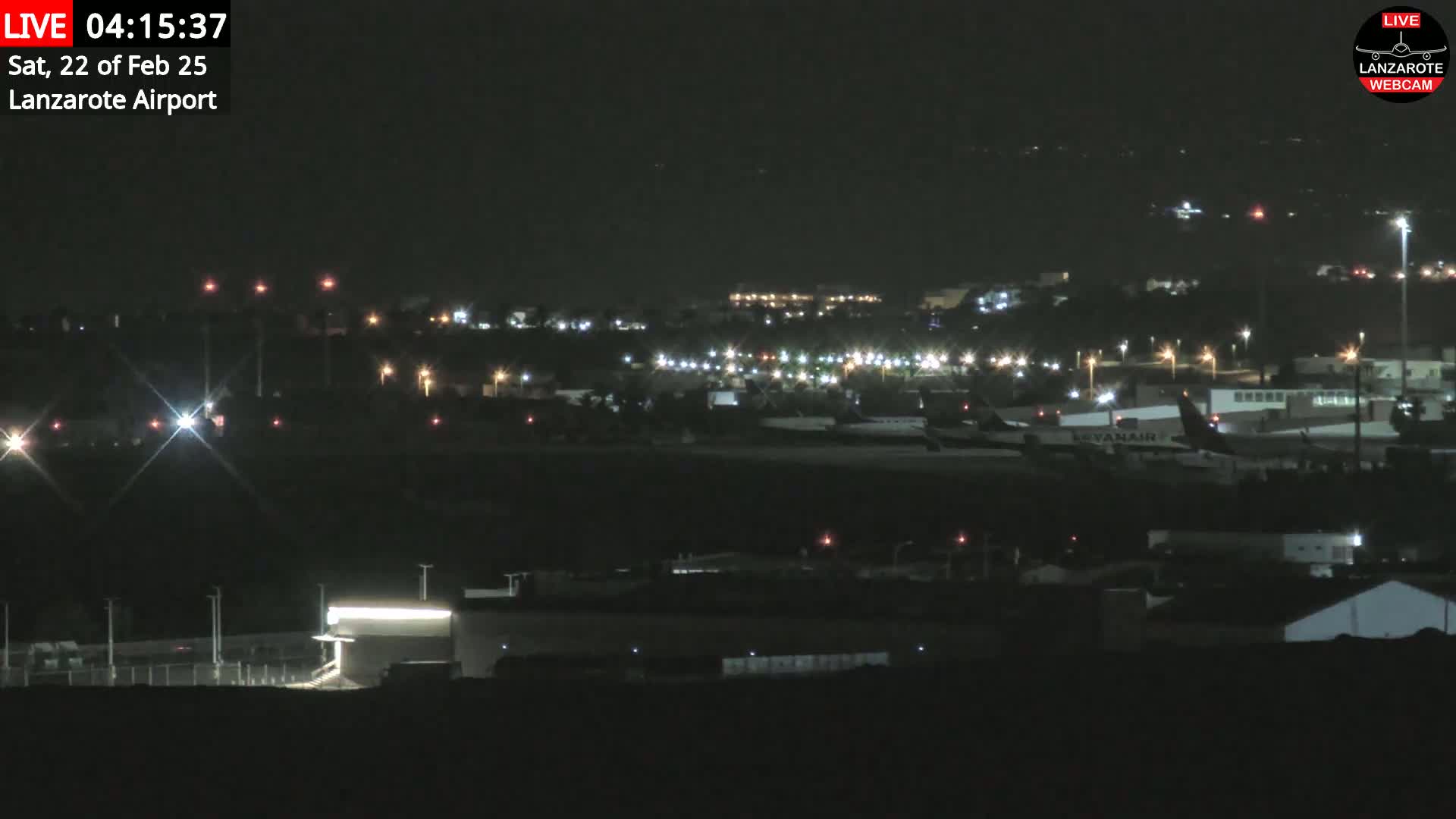 A nighttime, long-range view of an airport with several lights illuminating buildings and aircraft on the tarmac.
