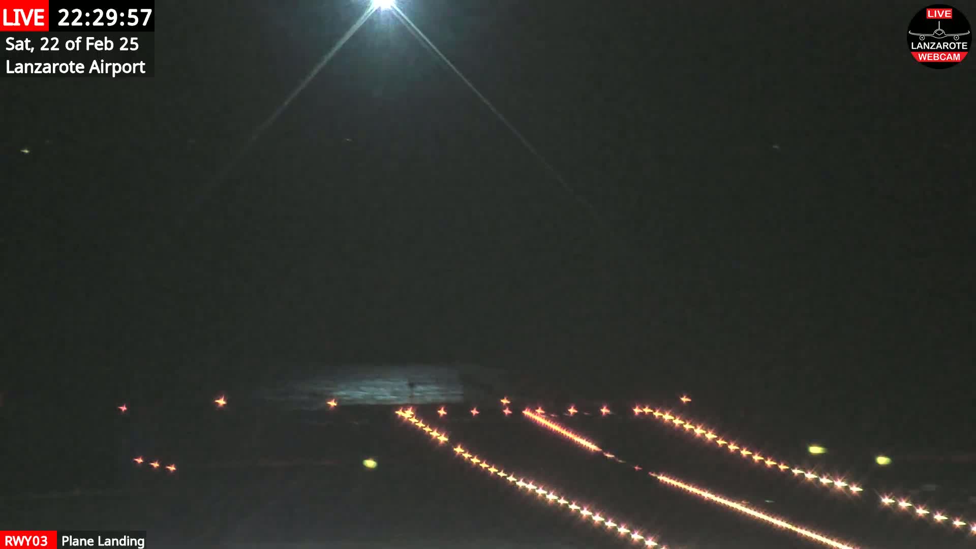 At night, a plane is landing on a runway illuminated by bright lights.