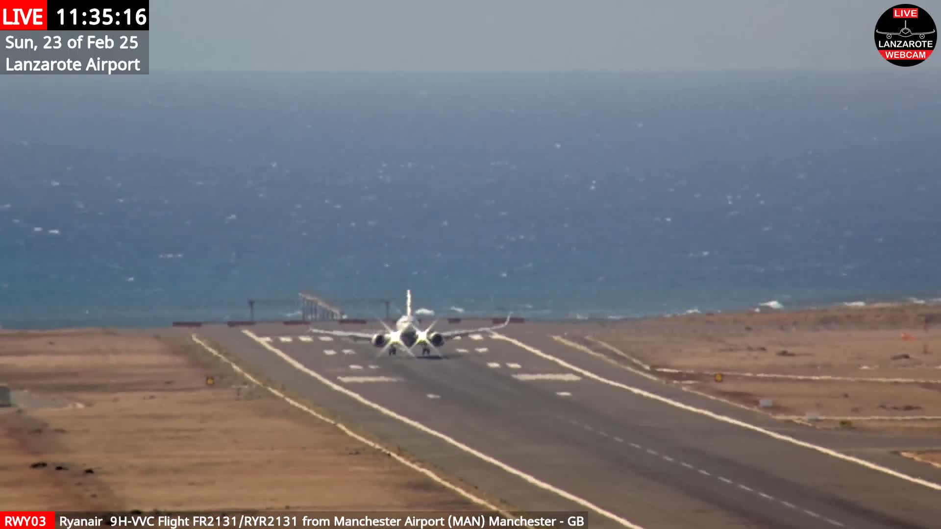 A passenger plane lands on a runway near a body of water under slightly windy conditions.