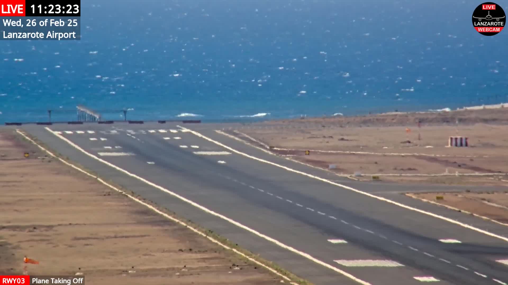A runway at an airport near a wavy ocean under a mostly clear sky.