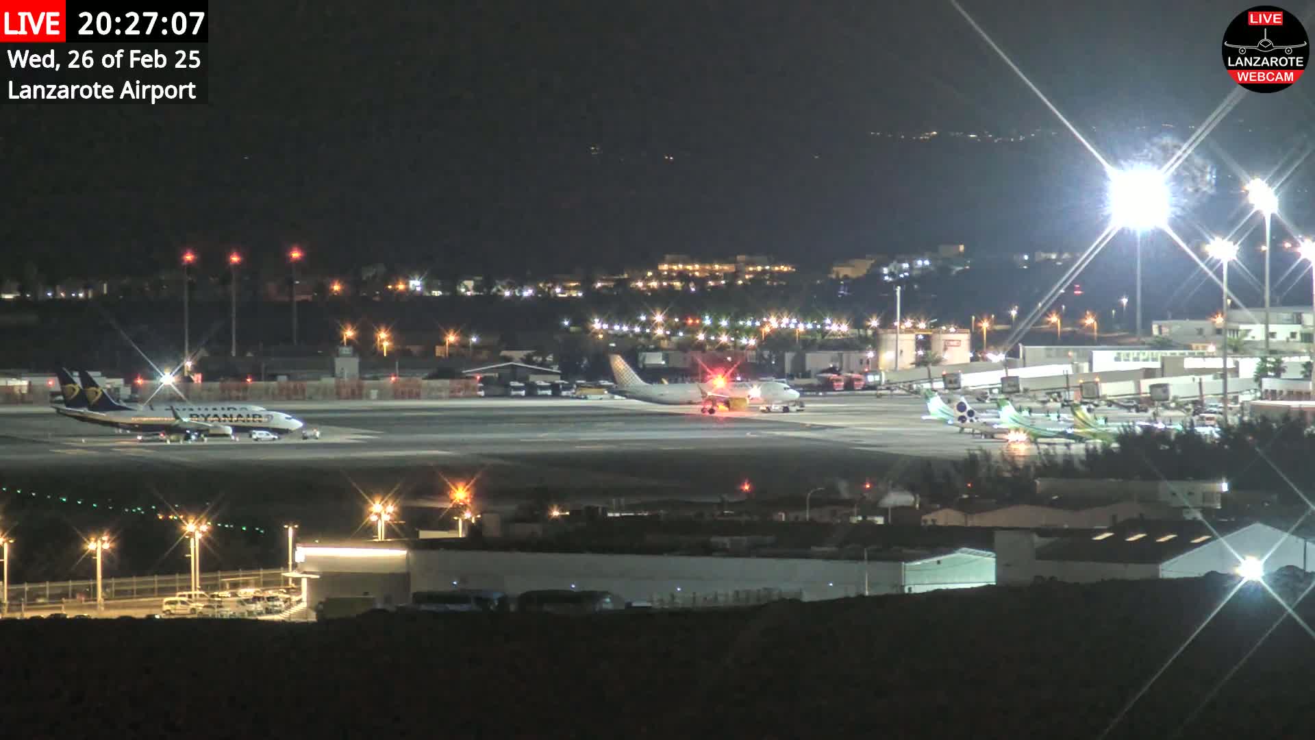 A nighttime view of an airport tarmac with several airplanes, illuminated by bright lights, under a clear, dark sky.