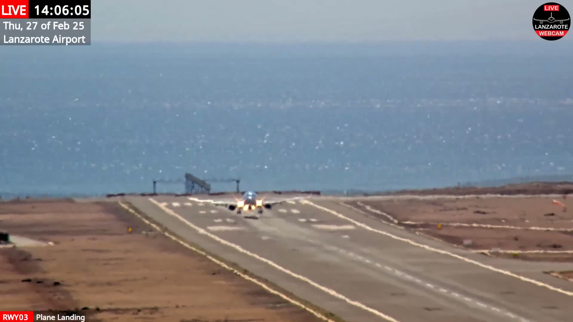 A plane is landing on a runway next to a body of water under a mostly clear sky.