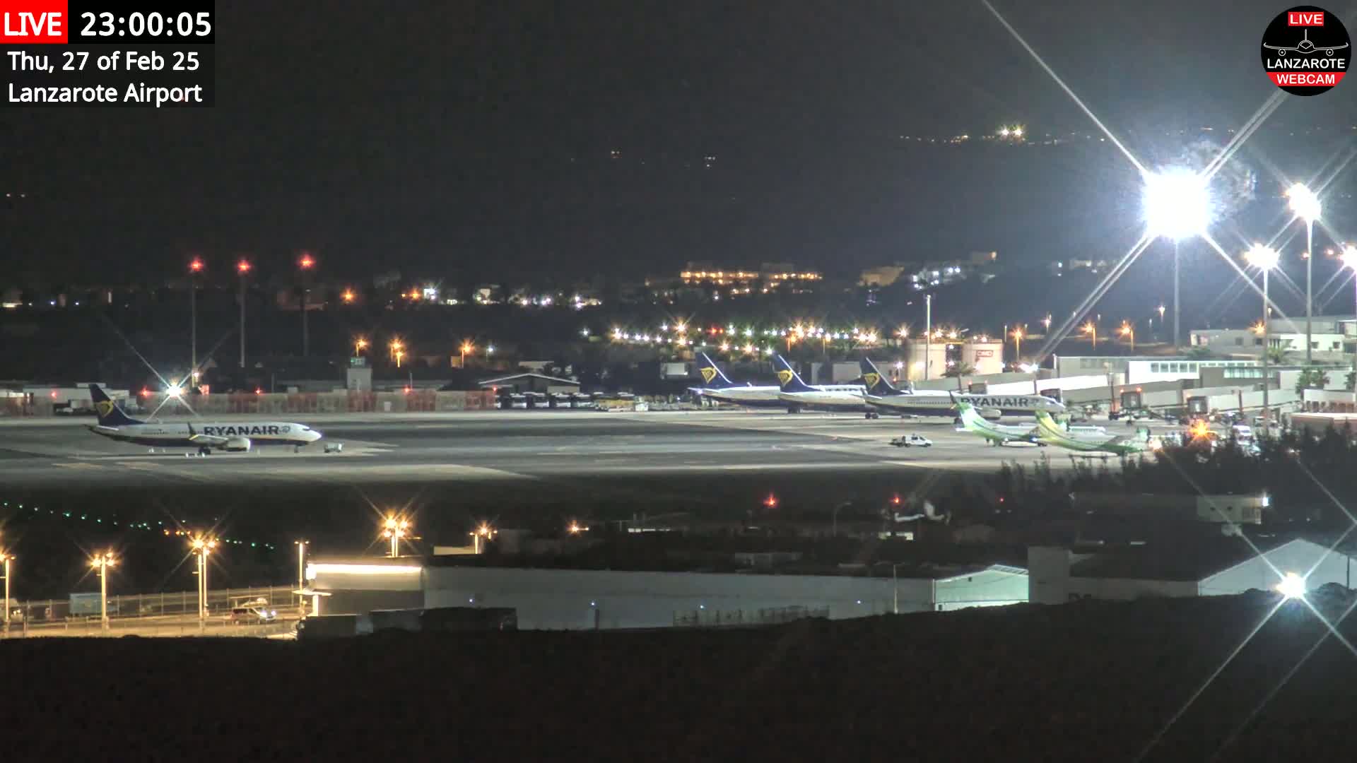 Several airplanes are parked on a brightly lit airport tarmac at night.