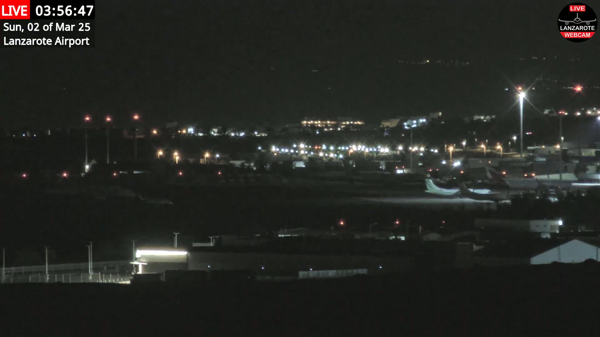 A nighttime view of an airport with airplanes on the tarmac and lights illuminating the surrounding area.