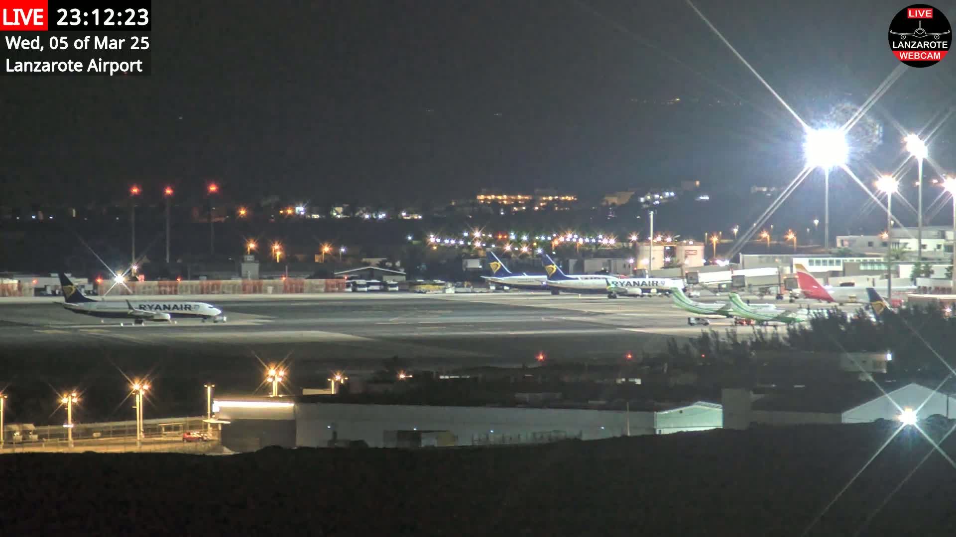 At night, several airplanes are parked on a brightly lit airport tarmac.