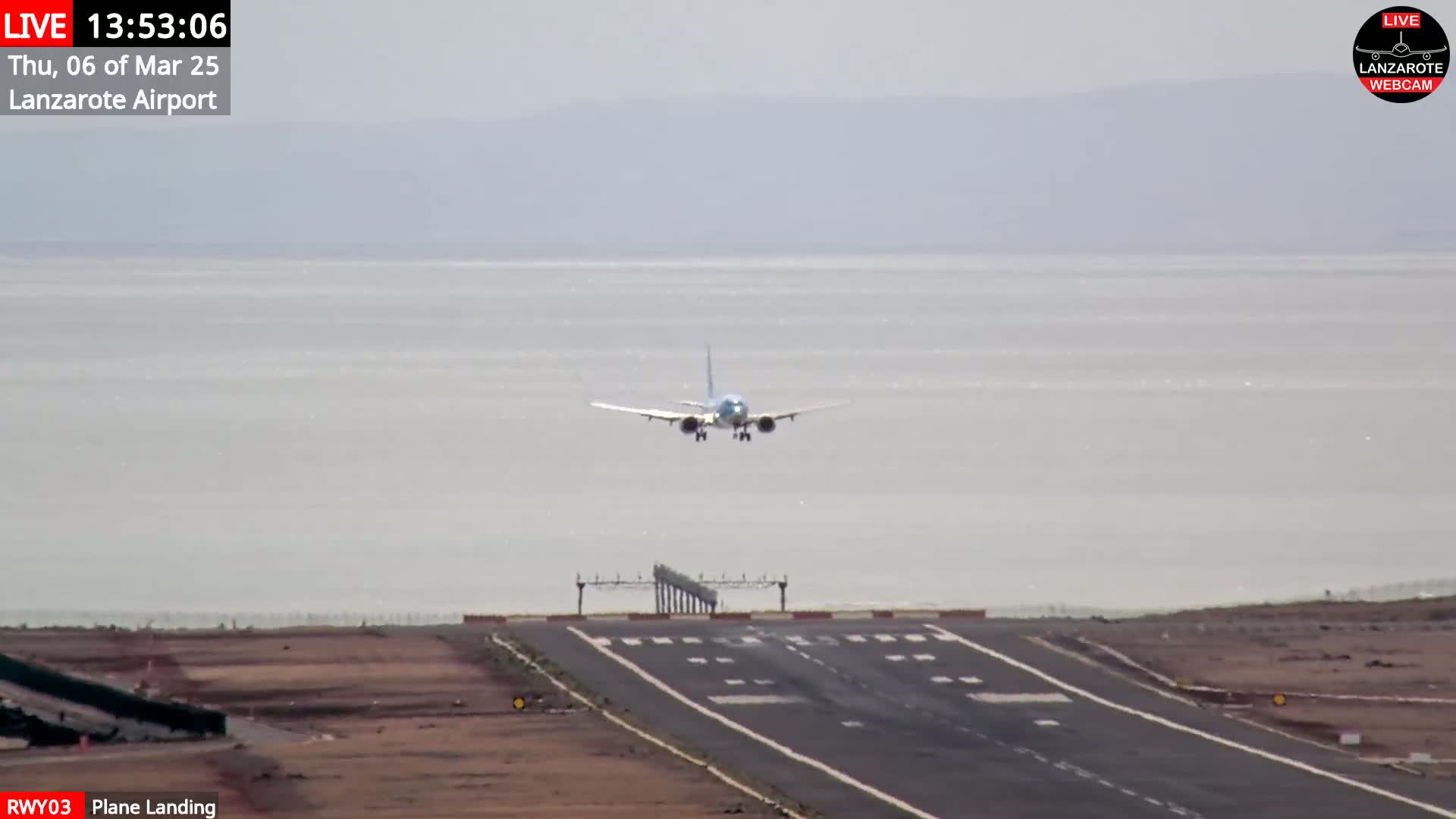 A passenger airplane is landing on a runway near a body of water under a hazy sky.