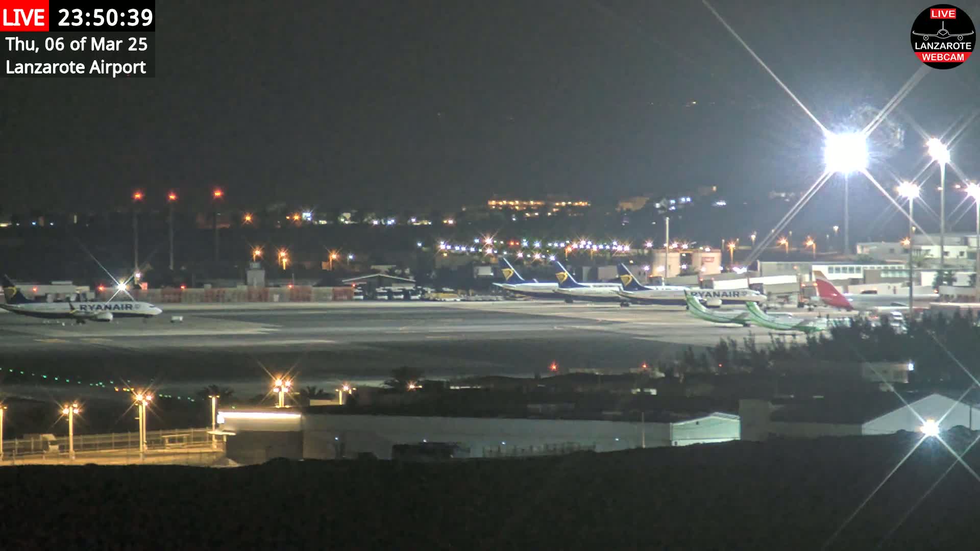 Several airplanes are parked on a brightly lit airport tarmac at night.
