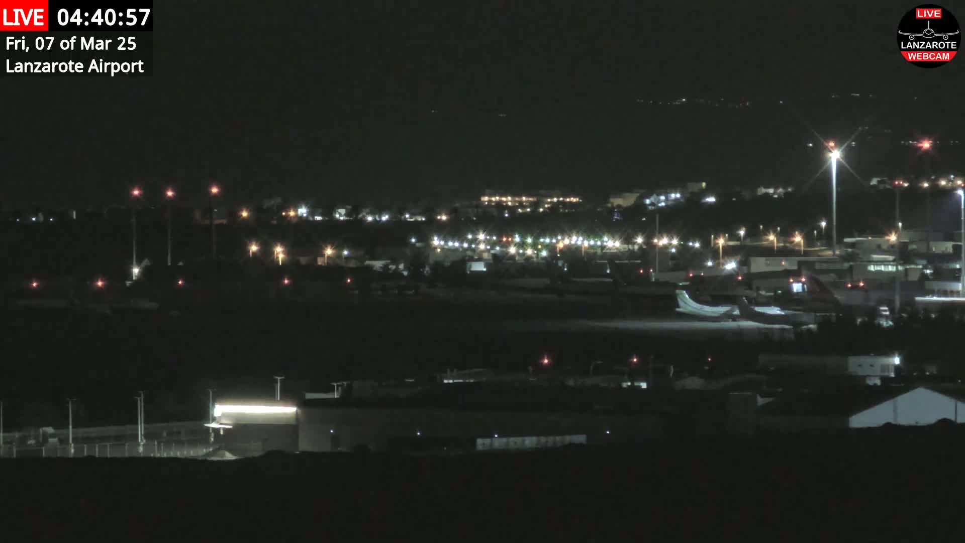 A nighttime long shot of an airport with a plane on the tarmac, under clear skies.