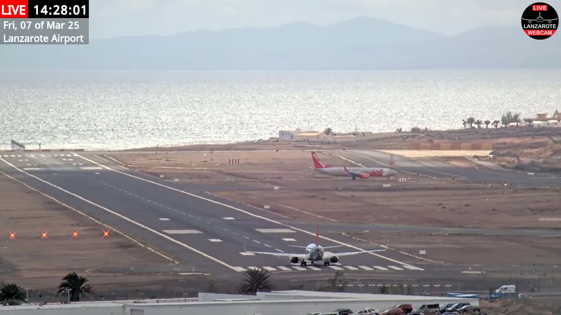 Two airplanes are on the tarmac of an airport near a body of water under a mostly clear sky.