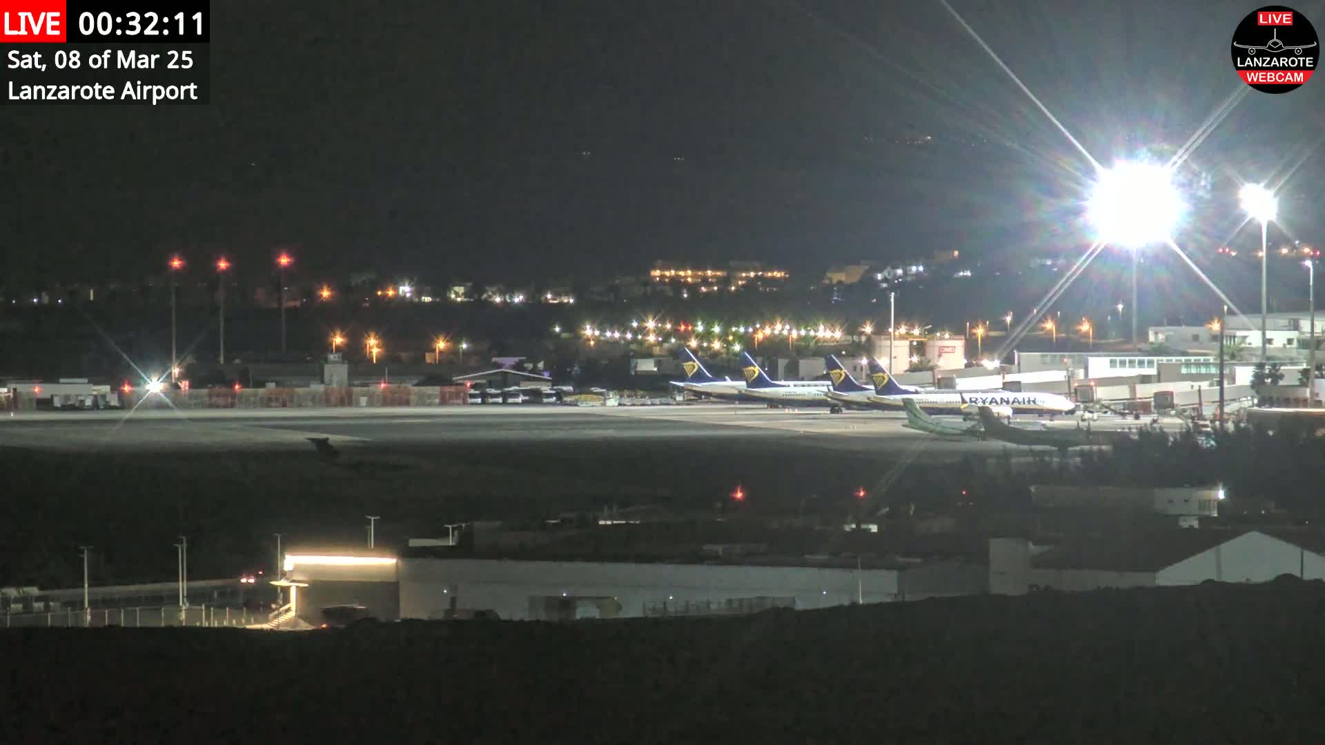 At night, several airplanes are parked on a brightly lit airport tarmac.
