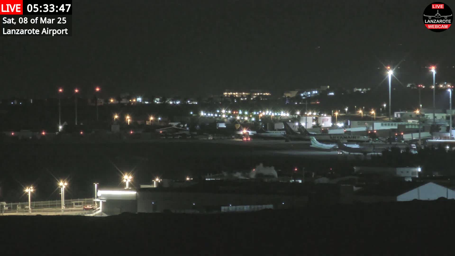 A nighttime view of an airport tarmac with several airplanes parked, illuminated by lights under a clear, dark sky.