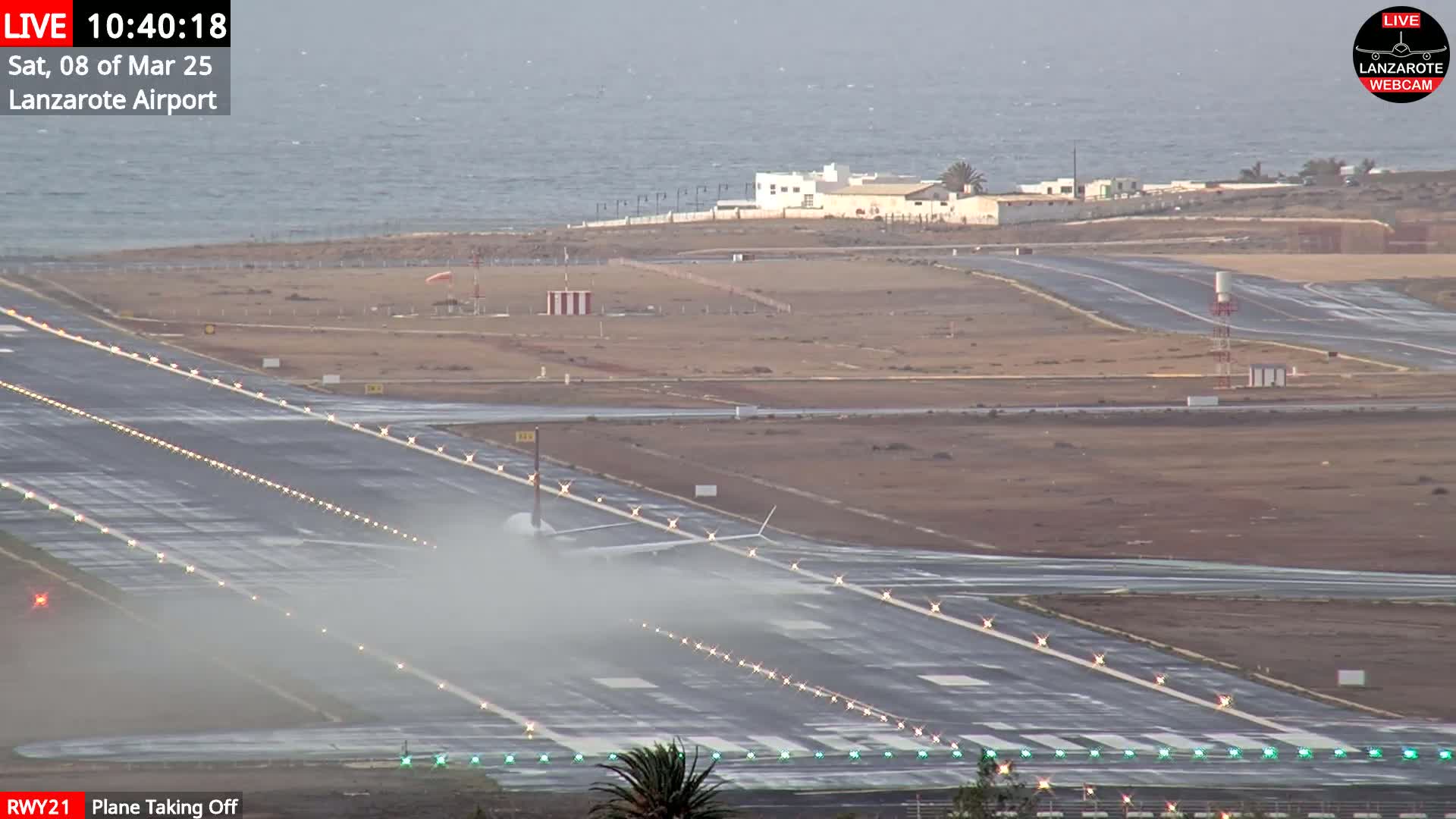 A plane is taking off from a runway near a body of water under overcast skies.