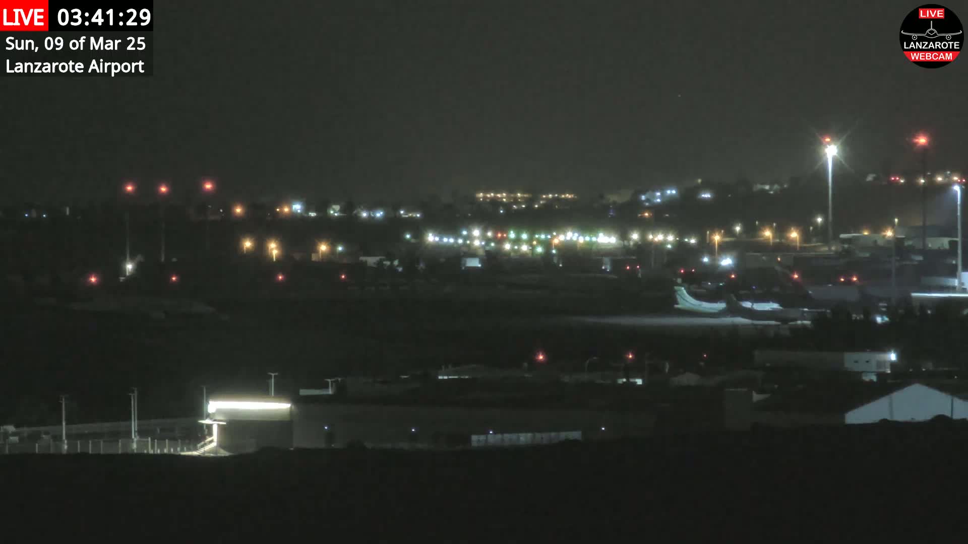 A nighttime view of an airport with lights illuminating the tarmac, runways, and surrounding buildings under a dark, clear sky.