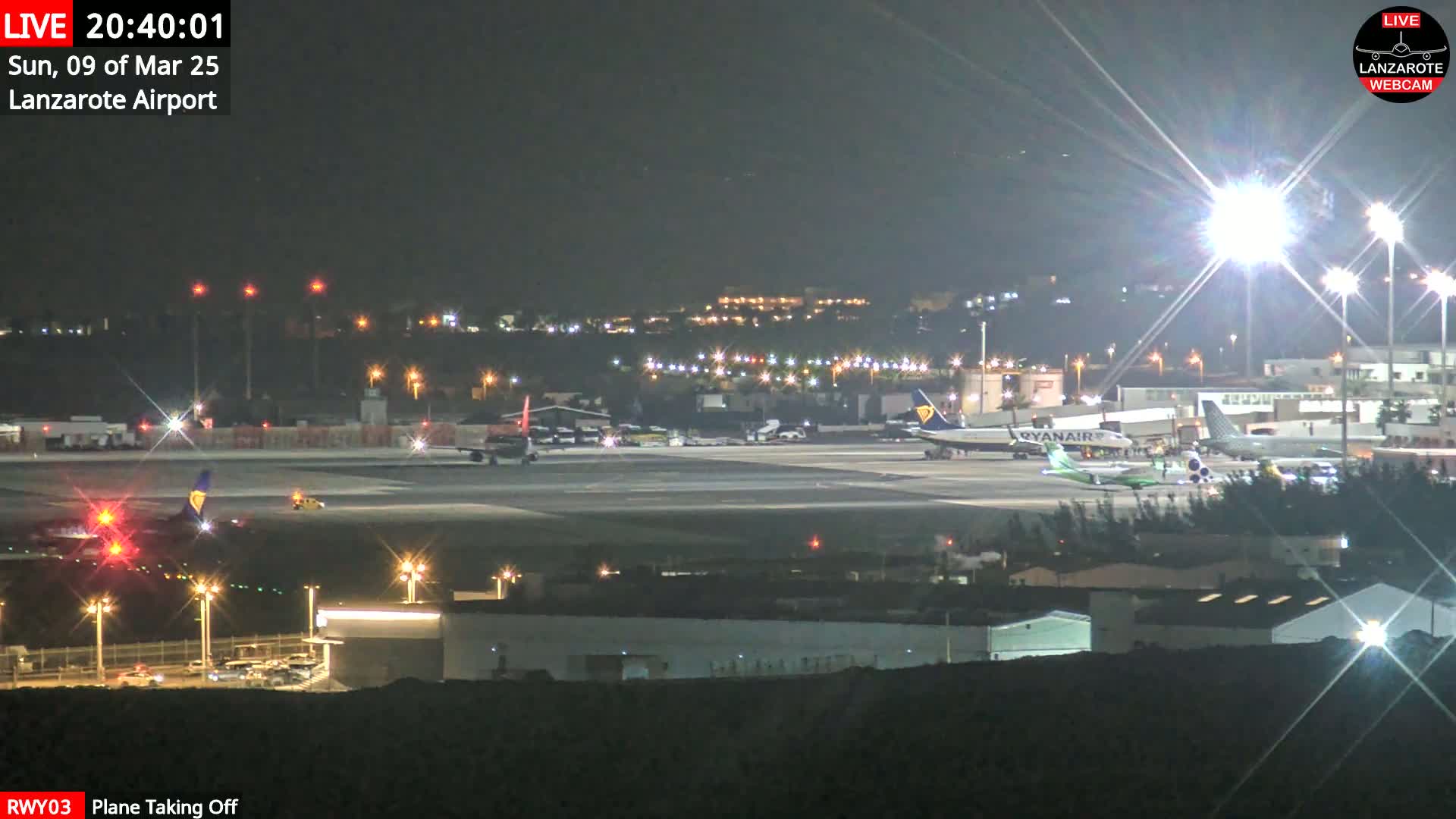 A nighttime view of an airport runway with several airplanes, one of which is taking off, under bright lights.