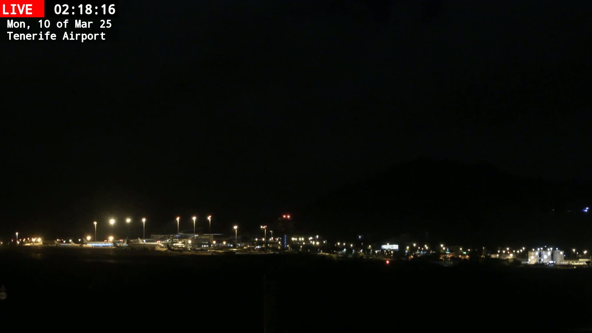A nighttime long shot of an airport with dimly lit buildings and runways under a dark sky.