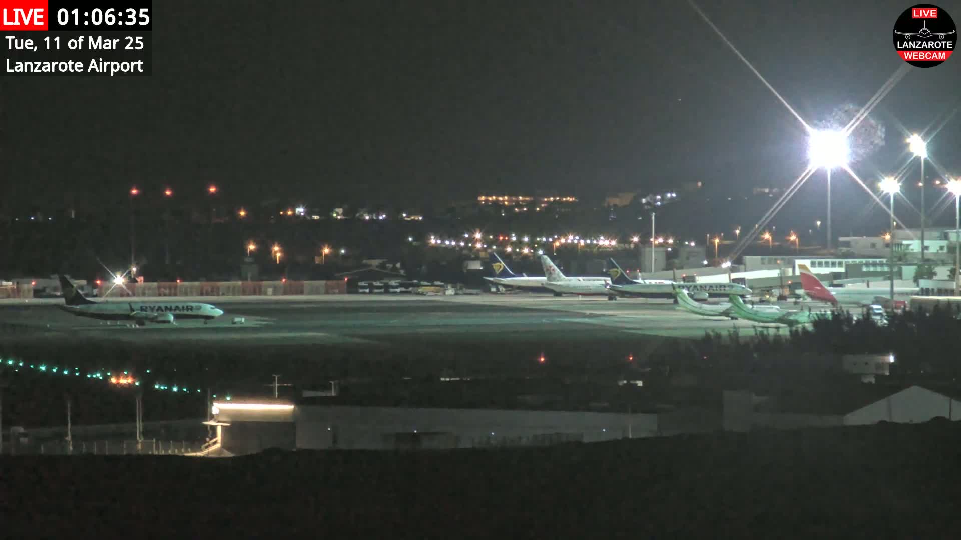 Several airplanes are parked on a brightly lit airport tarmac at night.