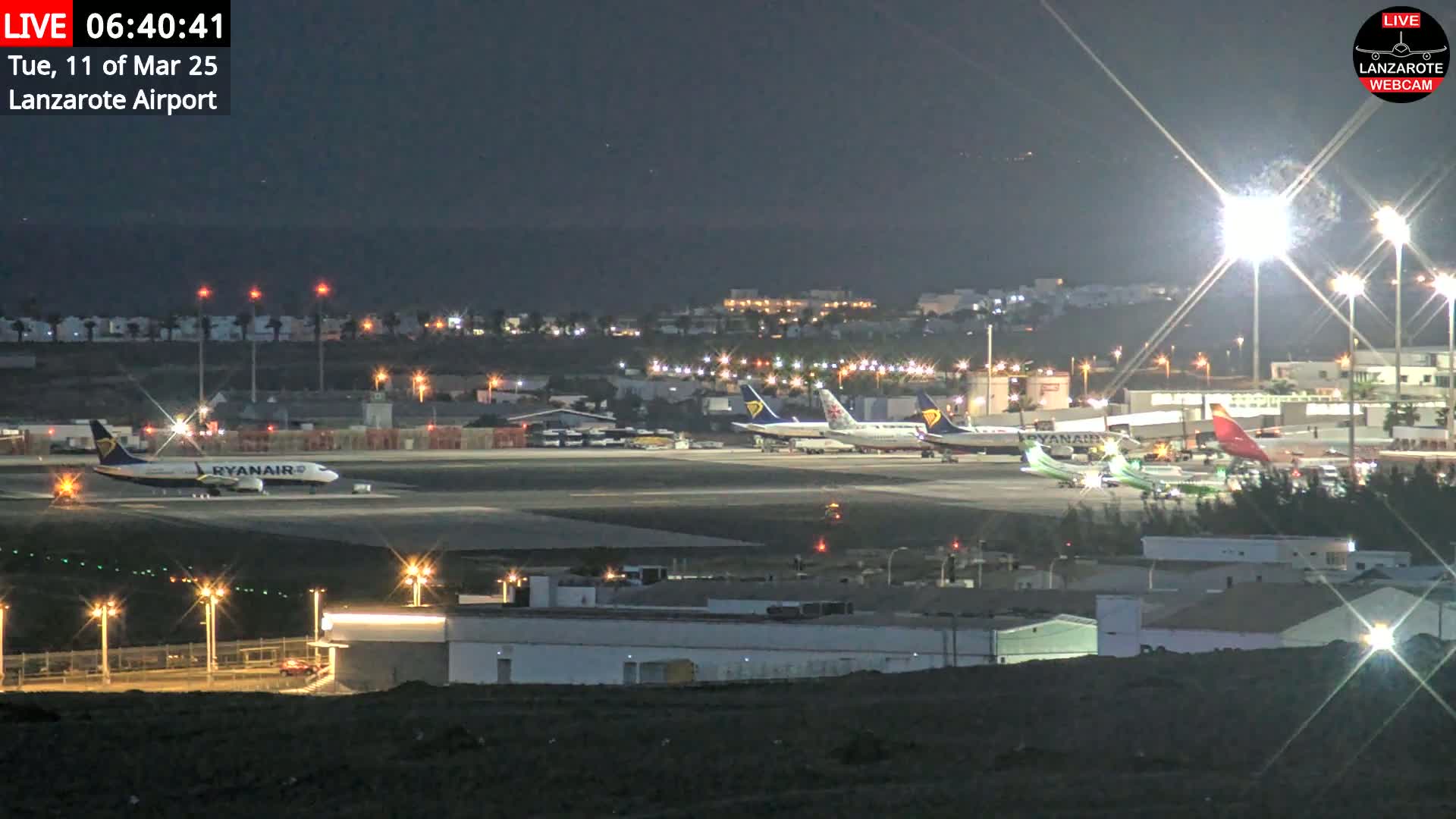 Several airplanes are parked on a brightly lit airport tarmac at night.