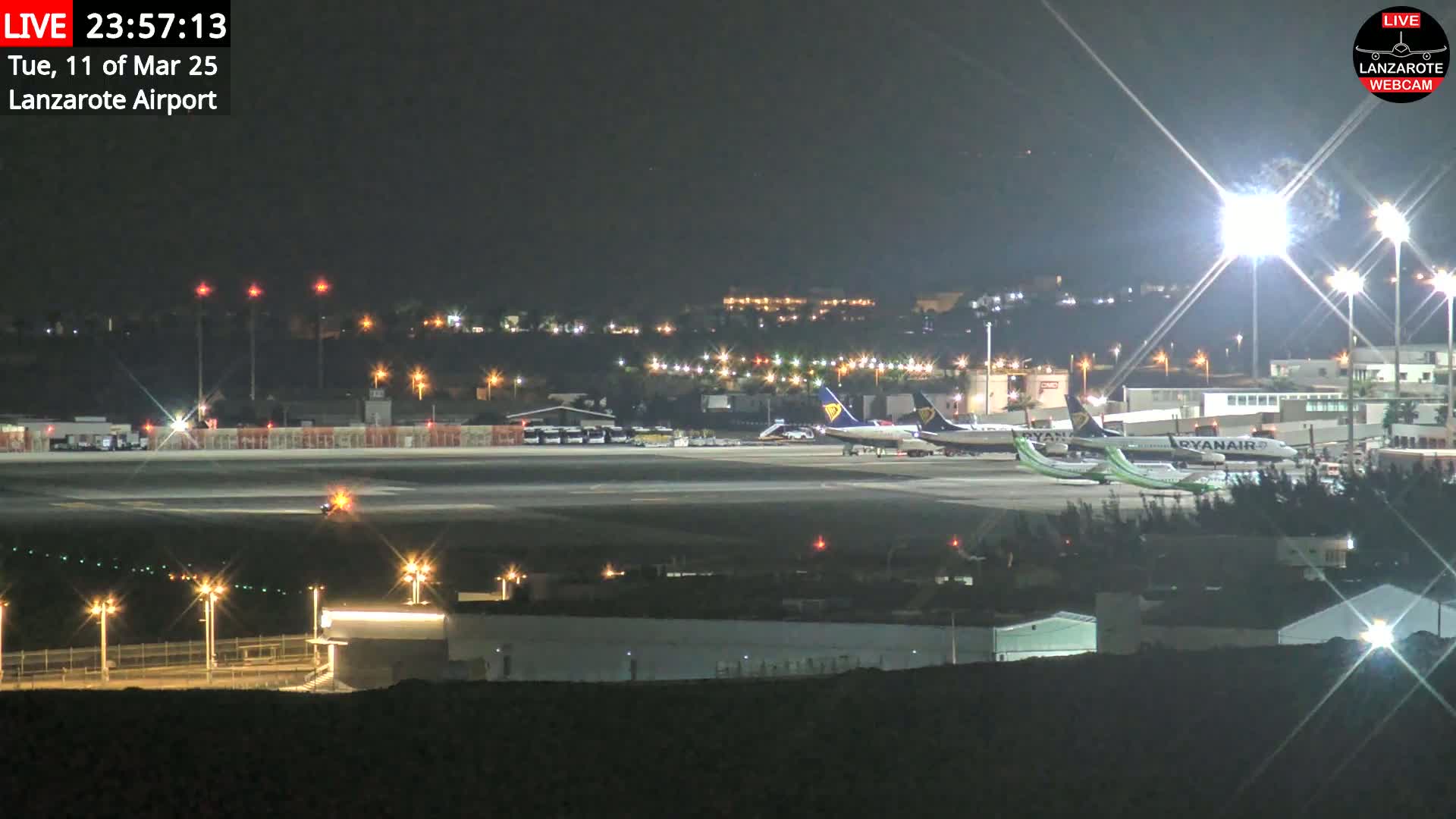 Several airplanes are parked on a brightly lit airport tarmac at night.
