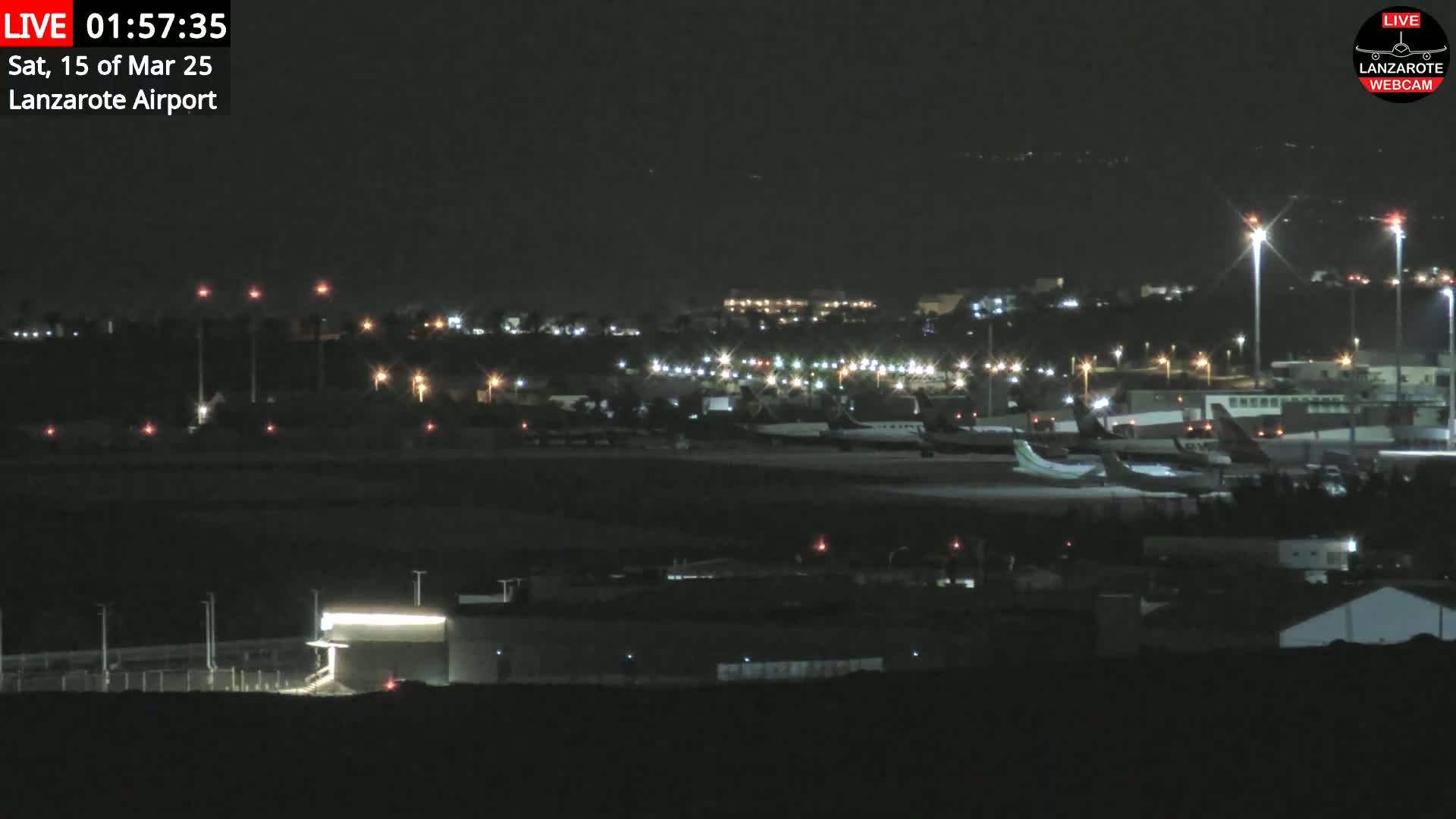 A nighttime view of an airport tarmac with several airplanes parked, illuminated by runway lights under a clear, dark sky.