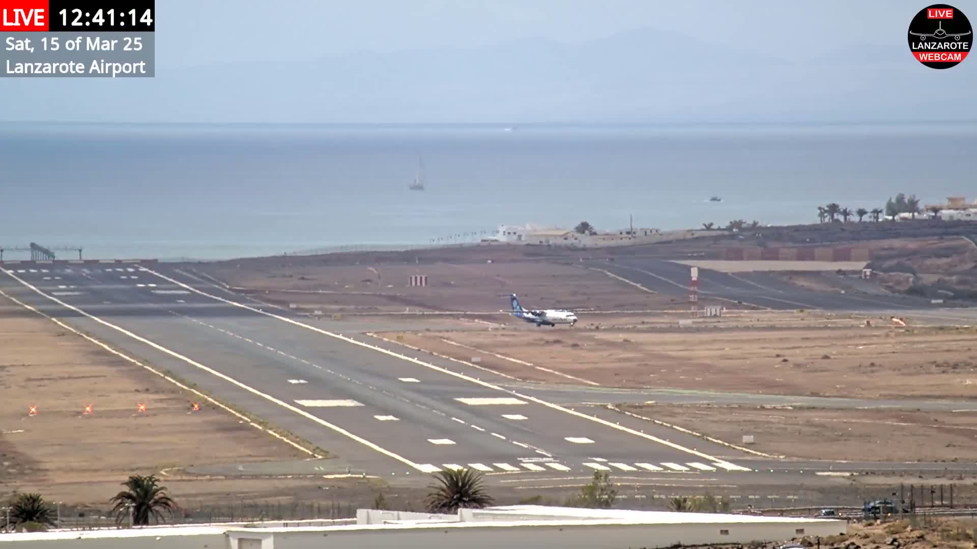 A small airplane is landing on a runway at an airport near a calm ocean under an overcast sky.