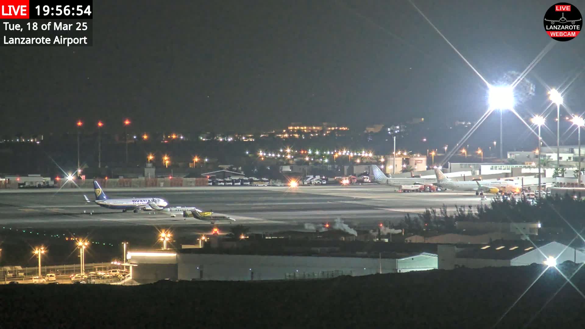 At night, several airplanes are parked on a brightly lit airport tarmac.