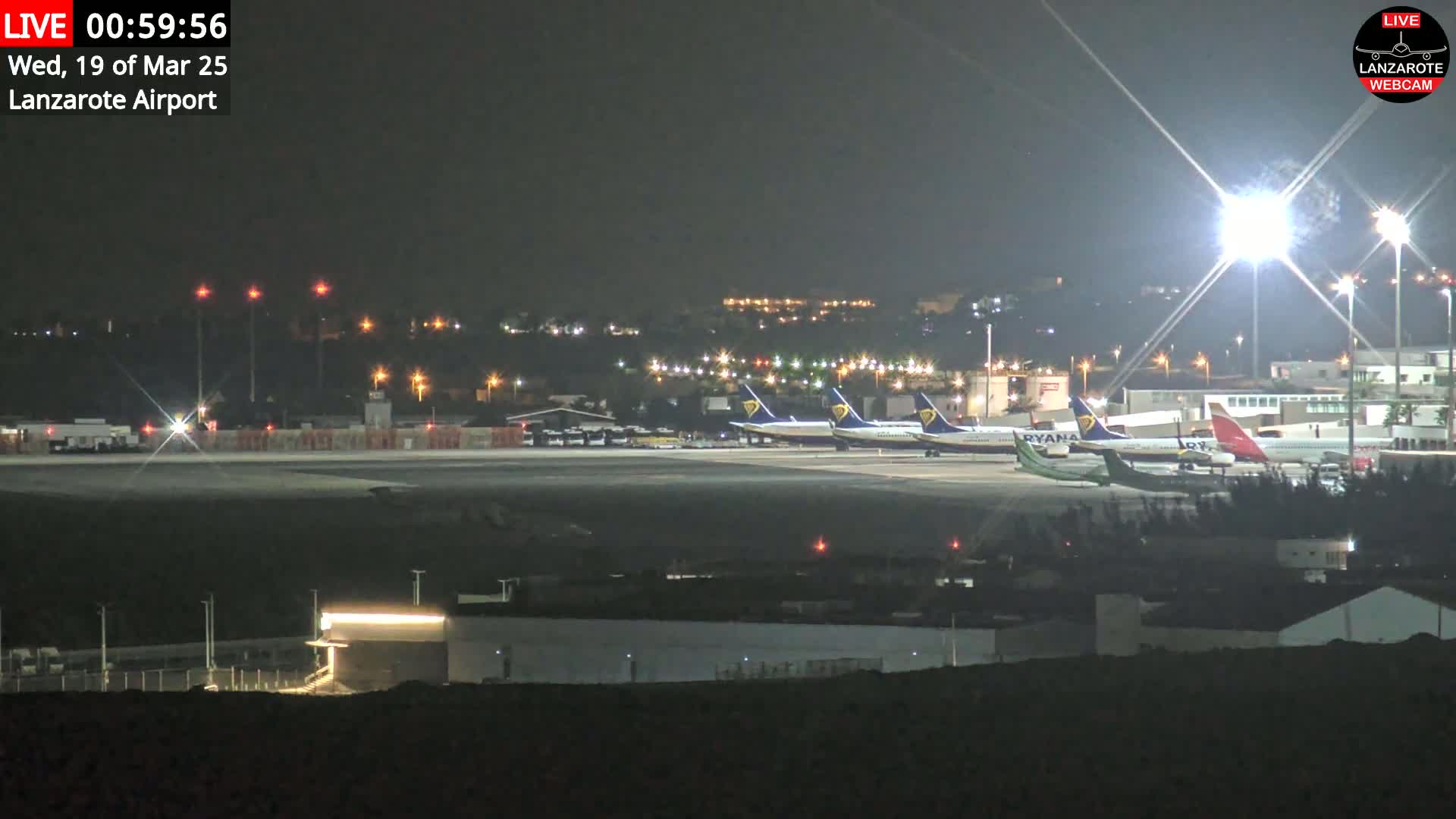 Several airplanes are parked on a brightly lit airport tarmac at night.