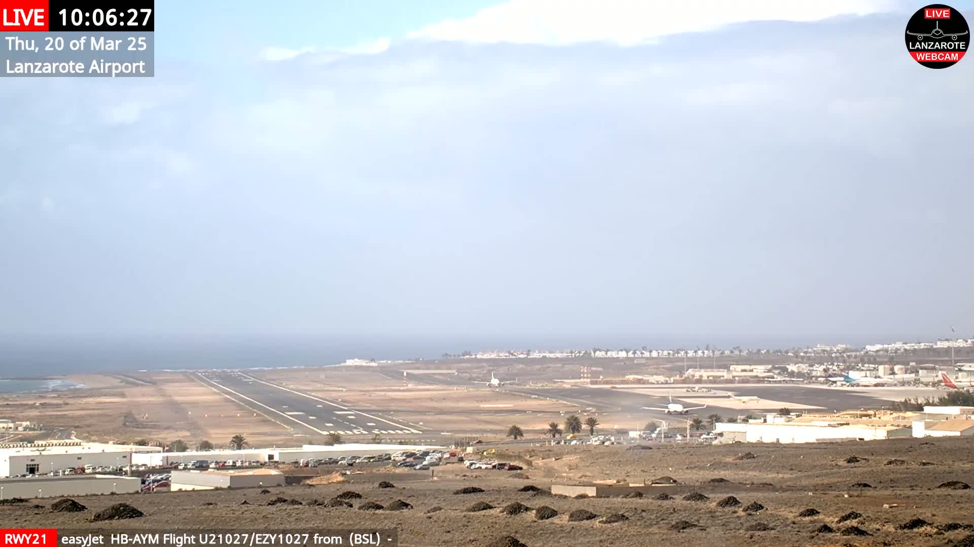 An airport runway and surrounding buildings are visible on a hazy day, with the ocean in the background.