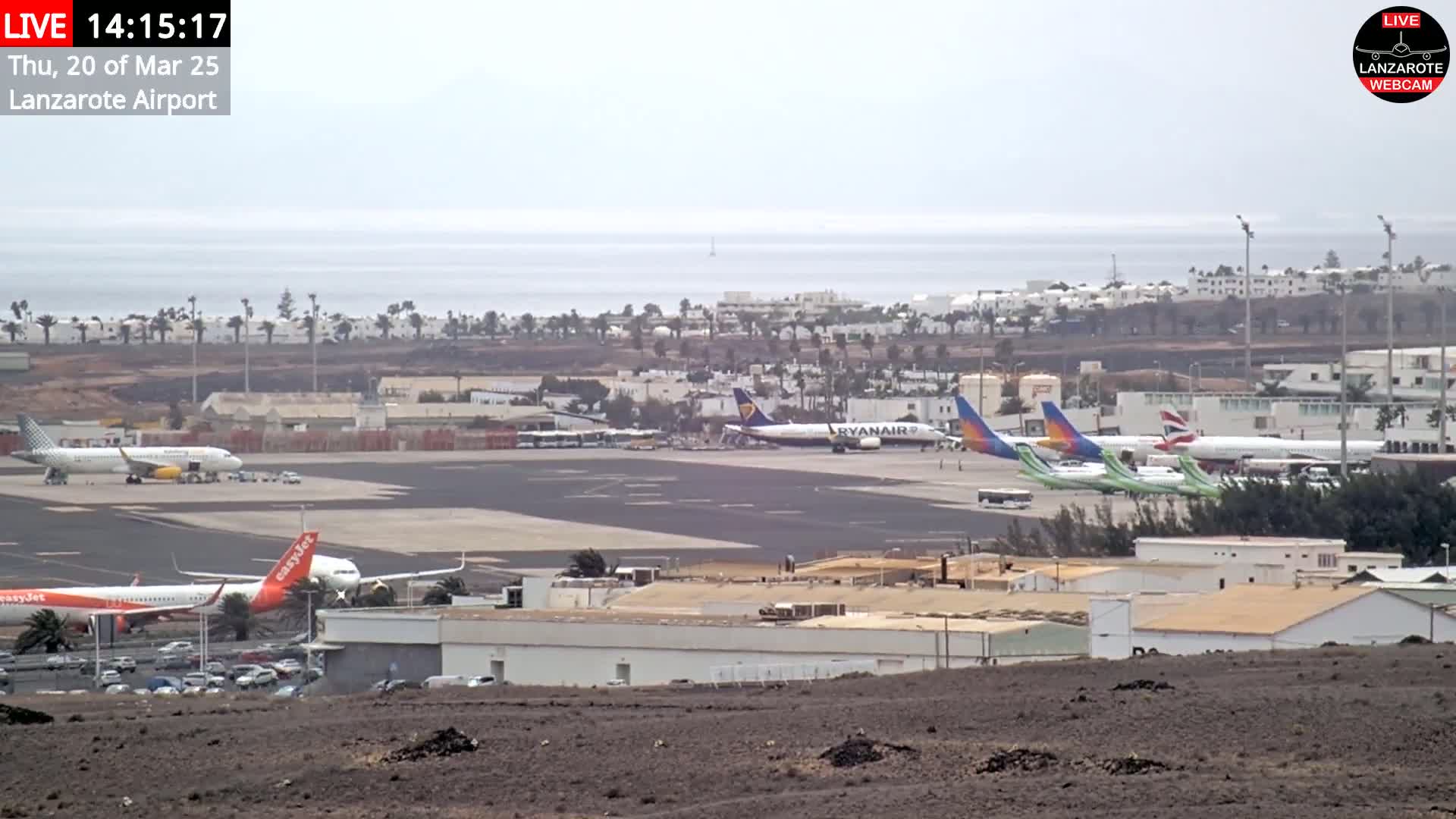 Several airplanes are parked on an airport tarmac on an overcast day near a body of water.