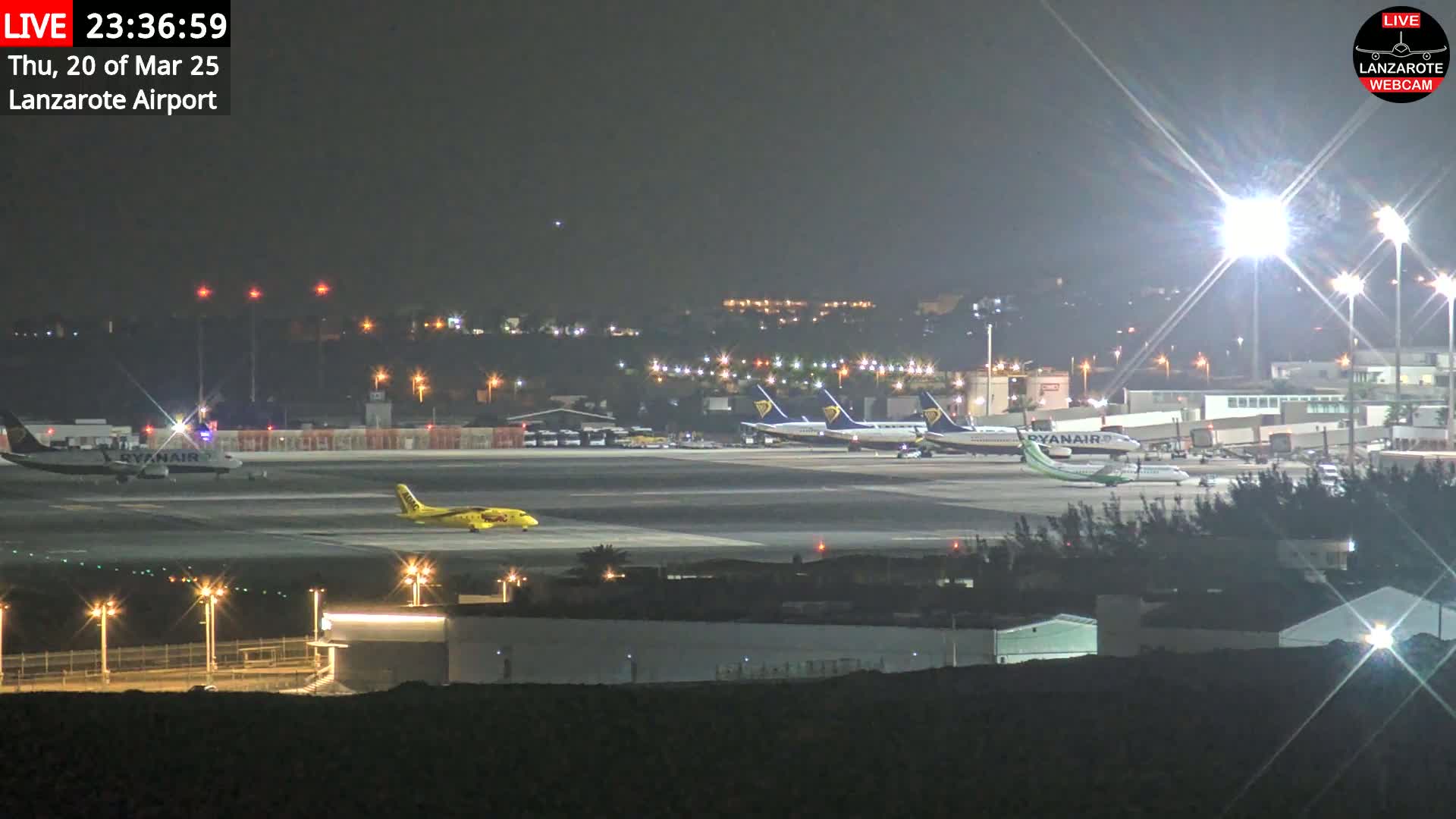 At night, several airplanes are parked on a brightly lit airport tarmac under a clear sky.