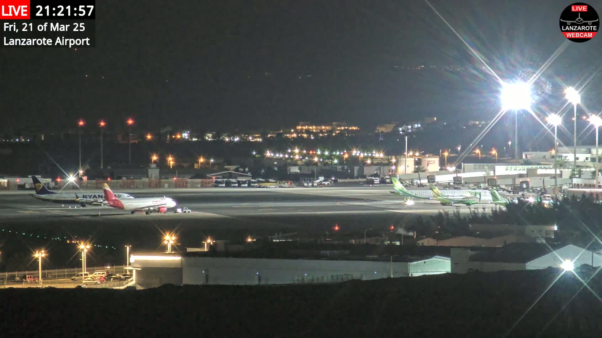 At night, two airplanes are parked on a brightly lit airport tarmac.