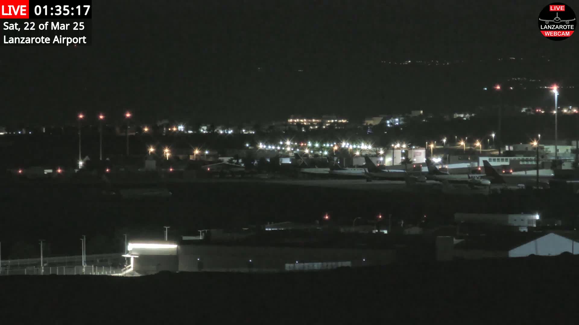 A nighttime view of an airport with several airplanes parked on the tarmac under a clear, dark sky.