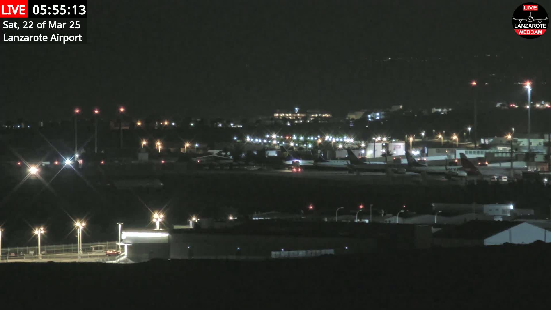 A nighttime view of an airport tarmac with several airplanes parked, illuminated by various lights under a clear, dark sky.