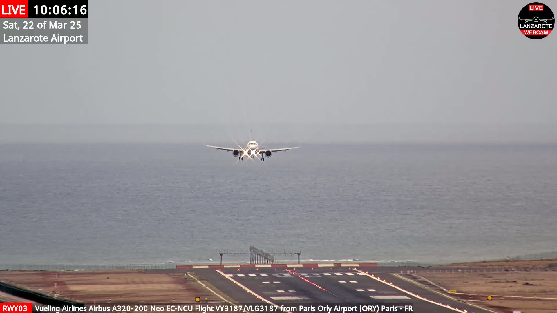 An airplane is landing on a runway next to a body of water under an overcast sky.