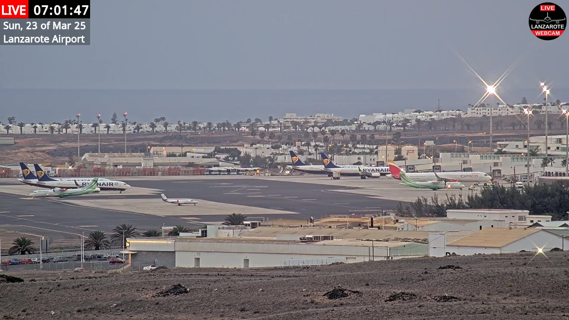 Several airplanes are parked on an airport tarmac near an ocean under an overcast sky.