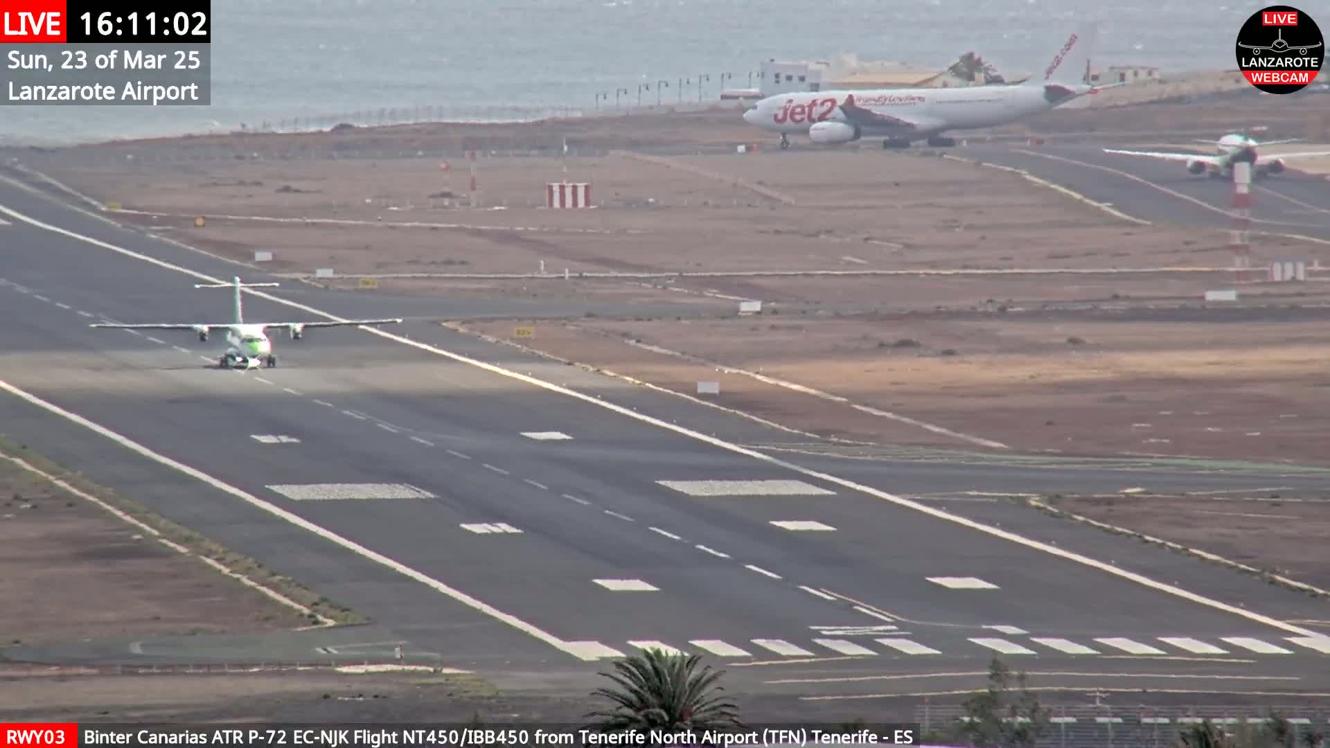 A small turboprop airplane taxis on a runway at an airport near a body of water under partly cloudy skies.