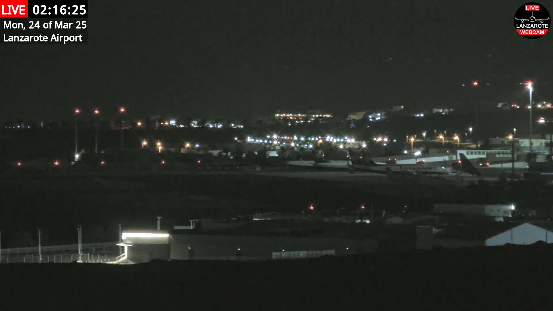 A nighttime long shot of an airport with several planes parked on the tarmac under a clear, dark sky.