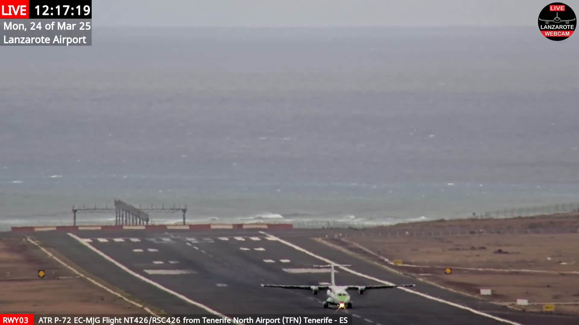 A small airplane taxis on a runway near a body of water under overcast skies.