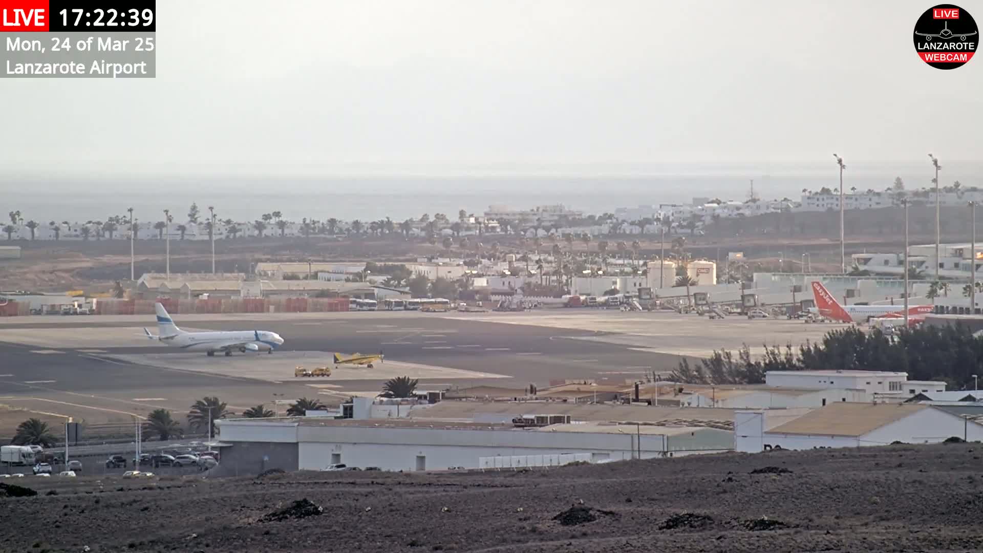 An airport with several airplanes on the tarmac is visible, with a hazy view of the ocean and distant buildings in the background.