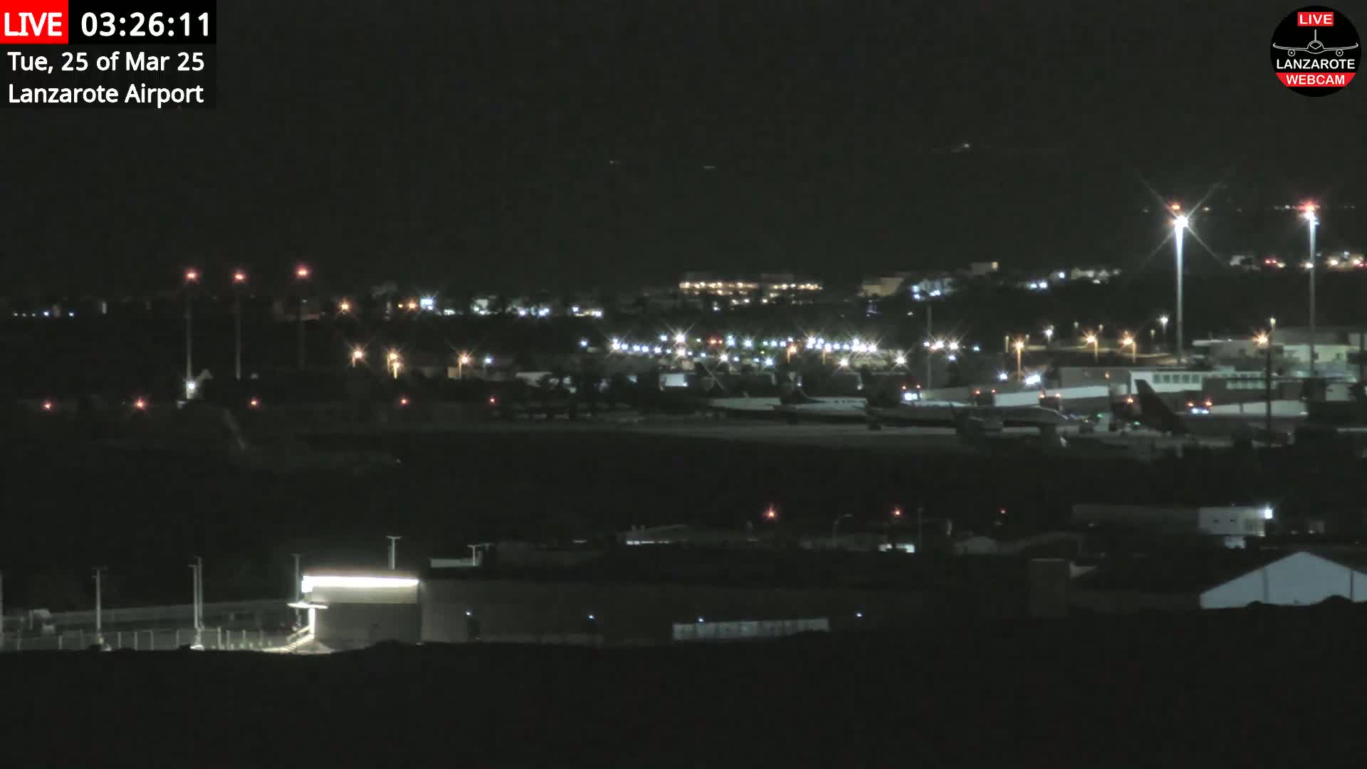 A nighttime long shot of an airport tarmac with several planes visible, under a clear, dark sky.
