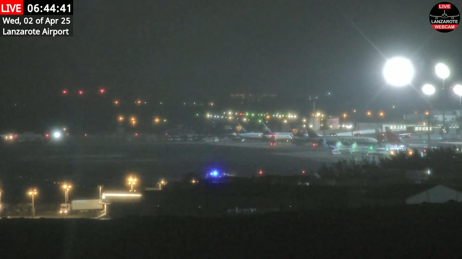 A nighttime view of an airport tarmac showing several airplanes and ground vehicles under hazy conditions.