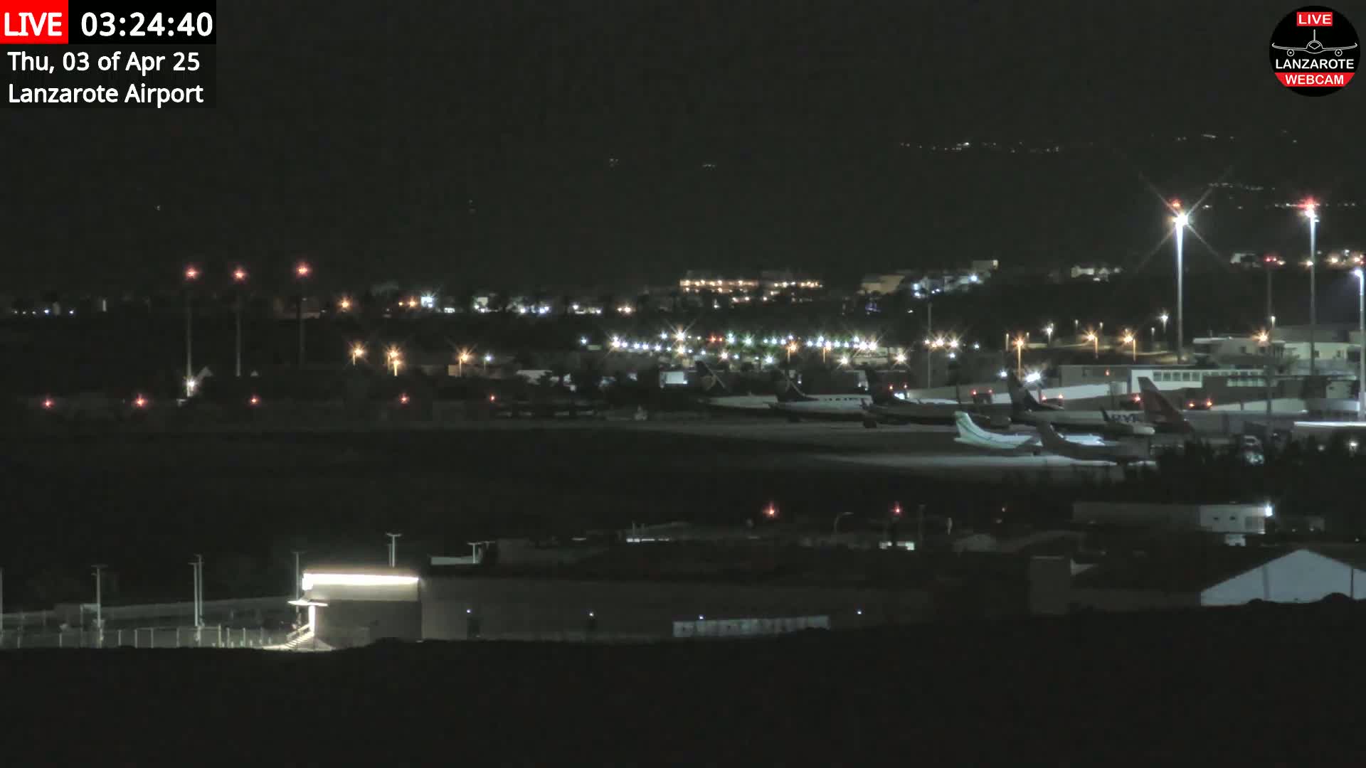 A nighttime long shot of an airport tarmac showing several airplanes parked under clear skies.