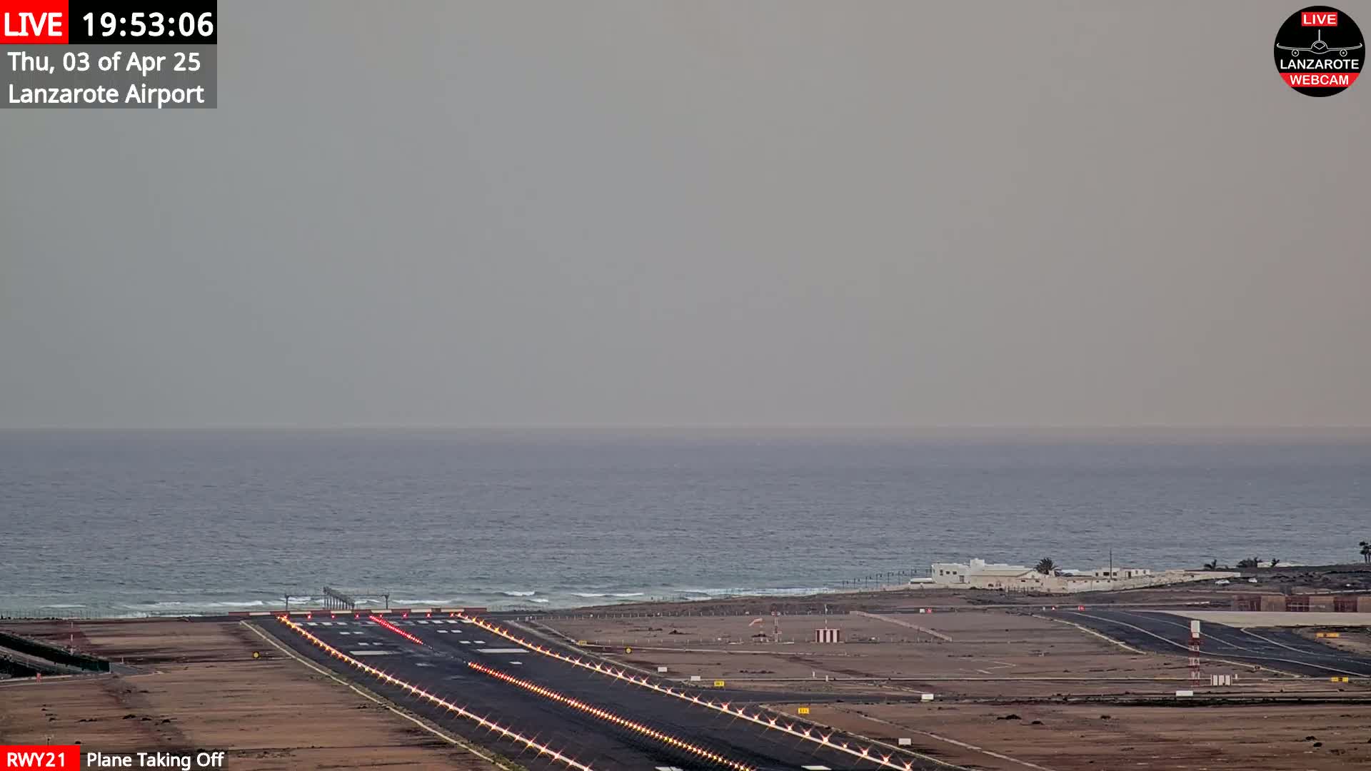 An airplane is taking off from a runway next to the ocean under hazy skies.