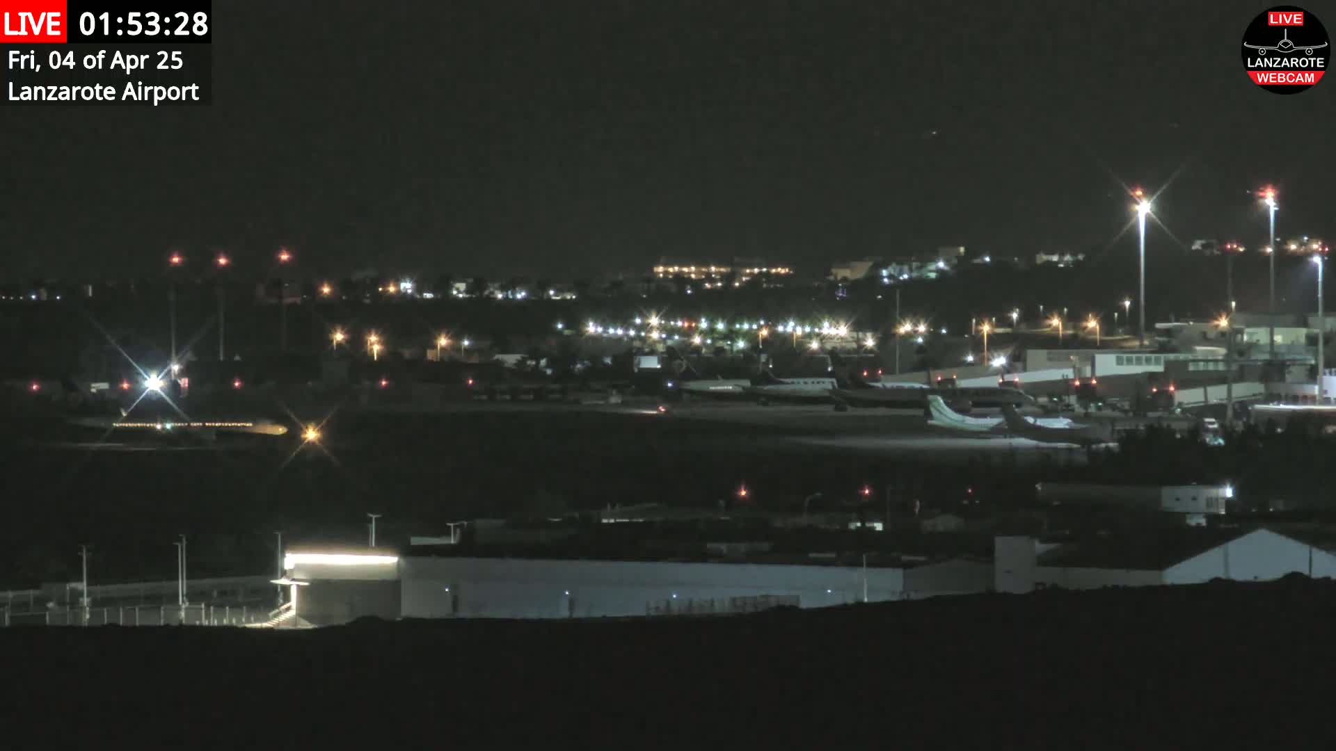 A nighttime view of an airport tarmac with several airplanes parked and illuminated by runway lights under a clear, dark sky.