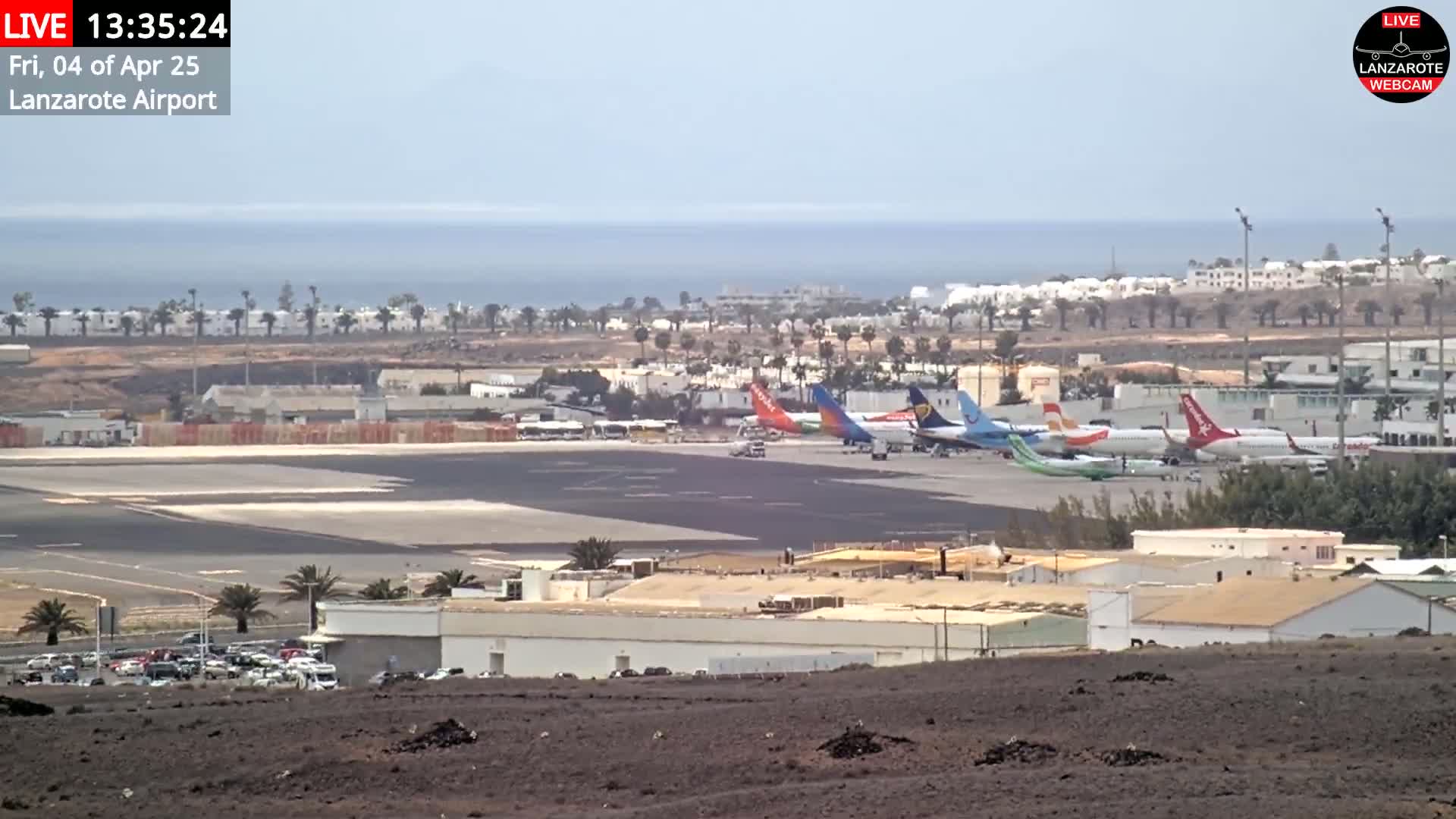 Several airplanes are parked on an airport tarmac near a coastline under a hazy sky.