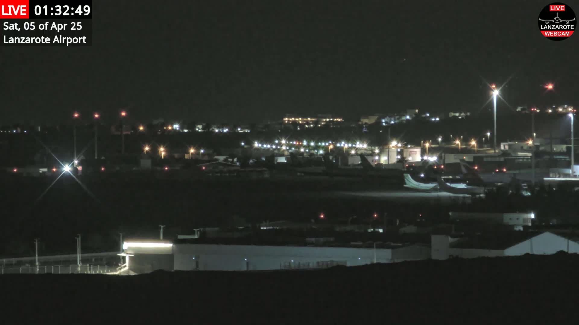 A nighttime view of an airport with numerous lights illuminating the tarmac, buildings, and surrounding area under a clear, dark sky.