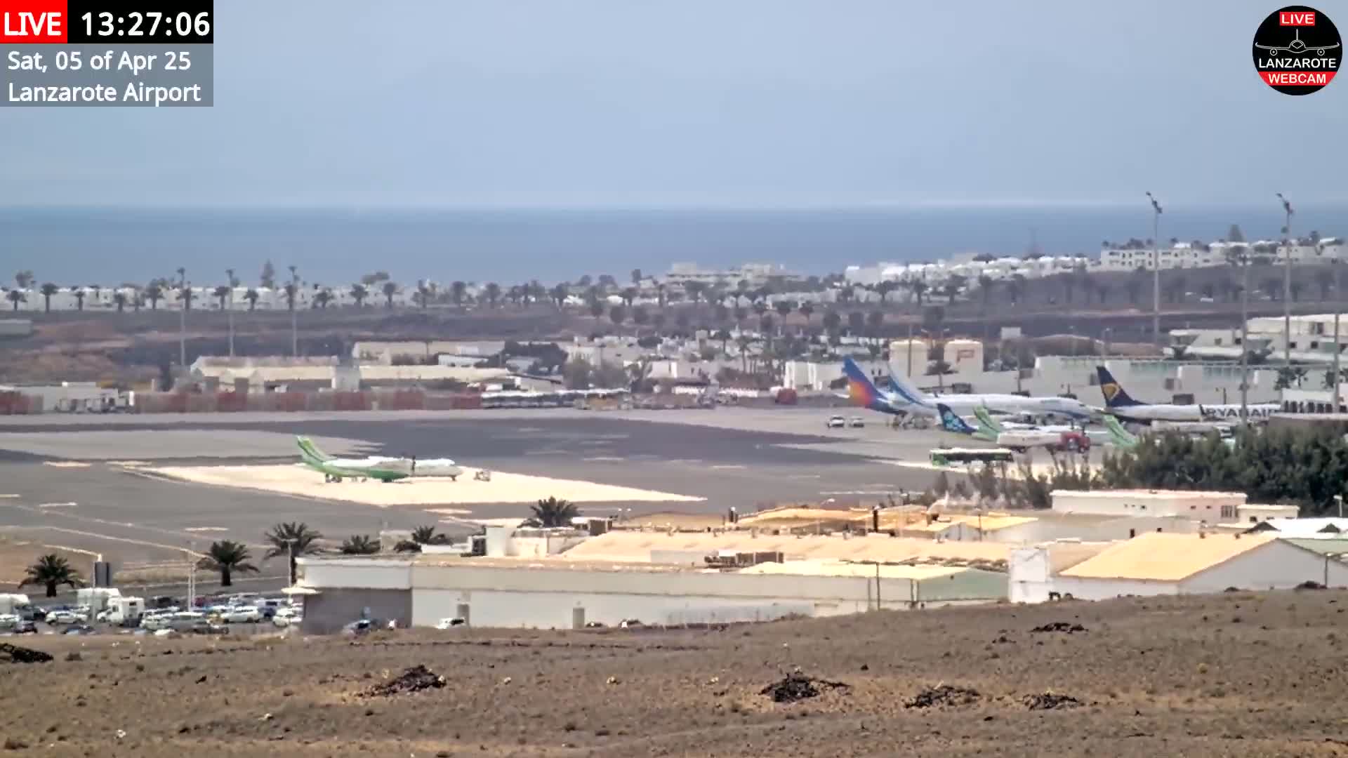 An airport tarmac with several airplanes is visible, overlooking a town and the ocean under a hazy sky.