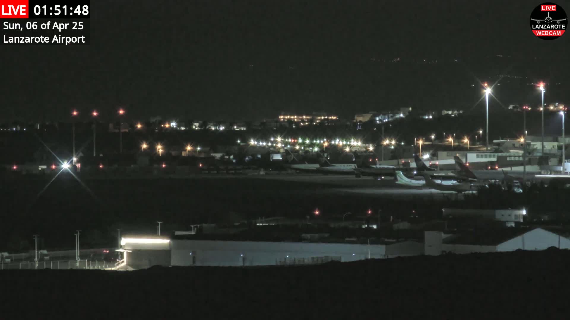 A nighttime view of an airport tarmac with several airplanes parked and illuminated, under a clear, dark sky.
