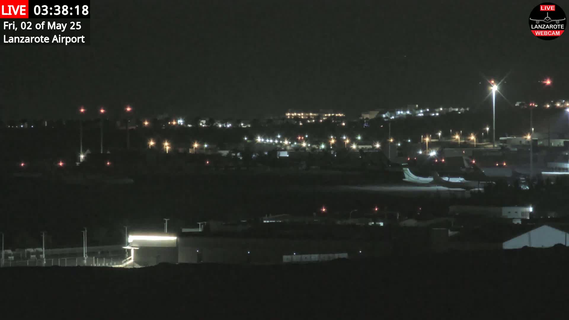 A nighttime long shot of an airport with scattered lights, under a clear, dark sky.