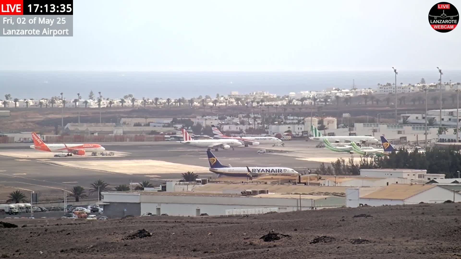 Several airplanes are parked on a tarmac at an airport near a calm ocean under a hazy sky.